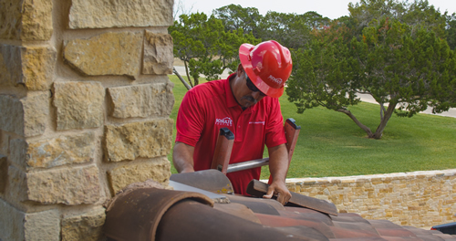 Schulte Roofing team member in a red uniform and hard hat working on a roof installation in San Antonio.