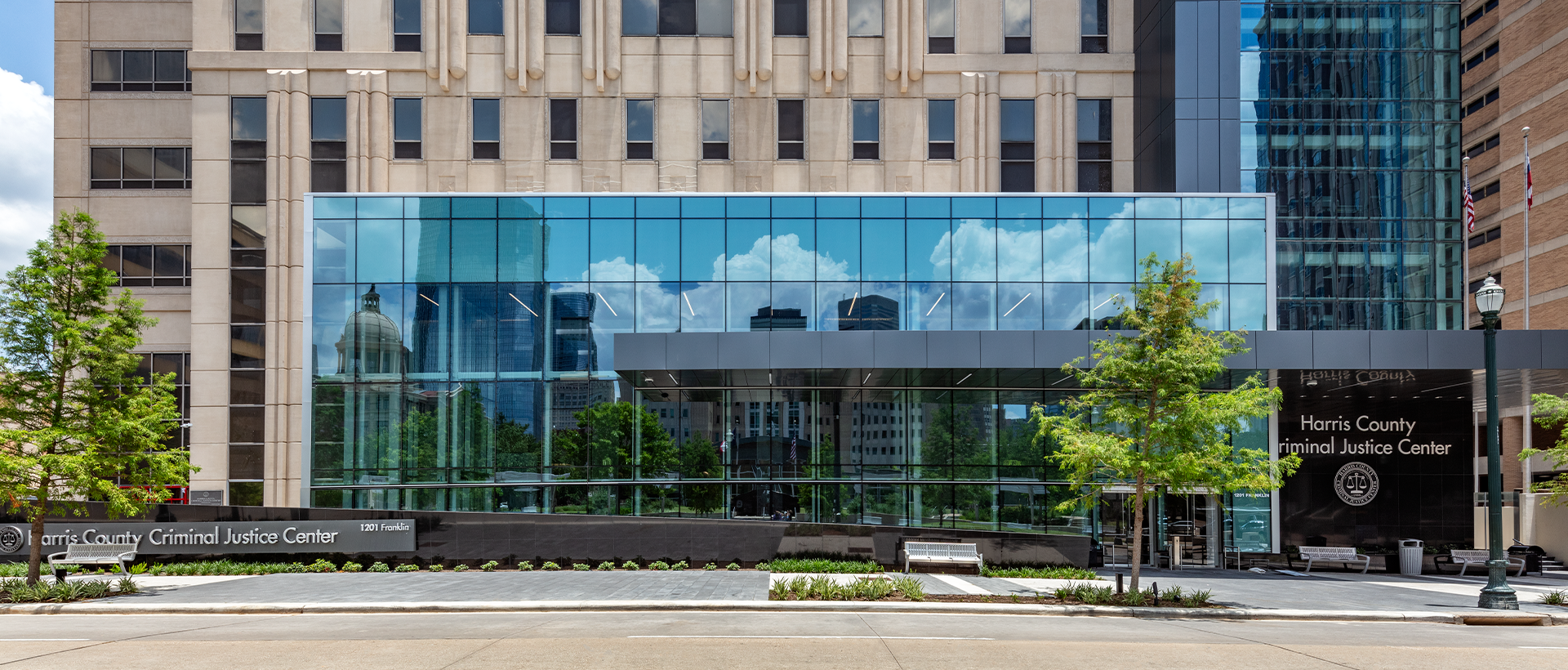 Criminal Justice Center - Schulte Roofing The Harris County Criminal Justice Center entryway from street view with the reflection of adjacent buildings in the window. Membrane roofing completed by Schulte Roofing.