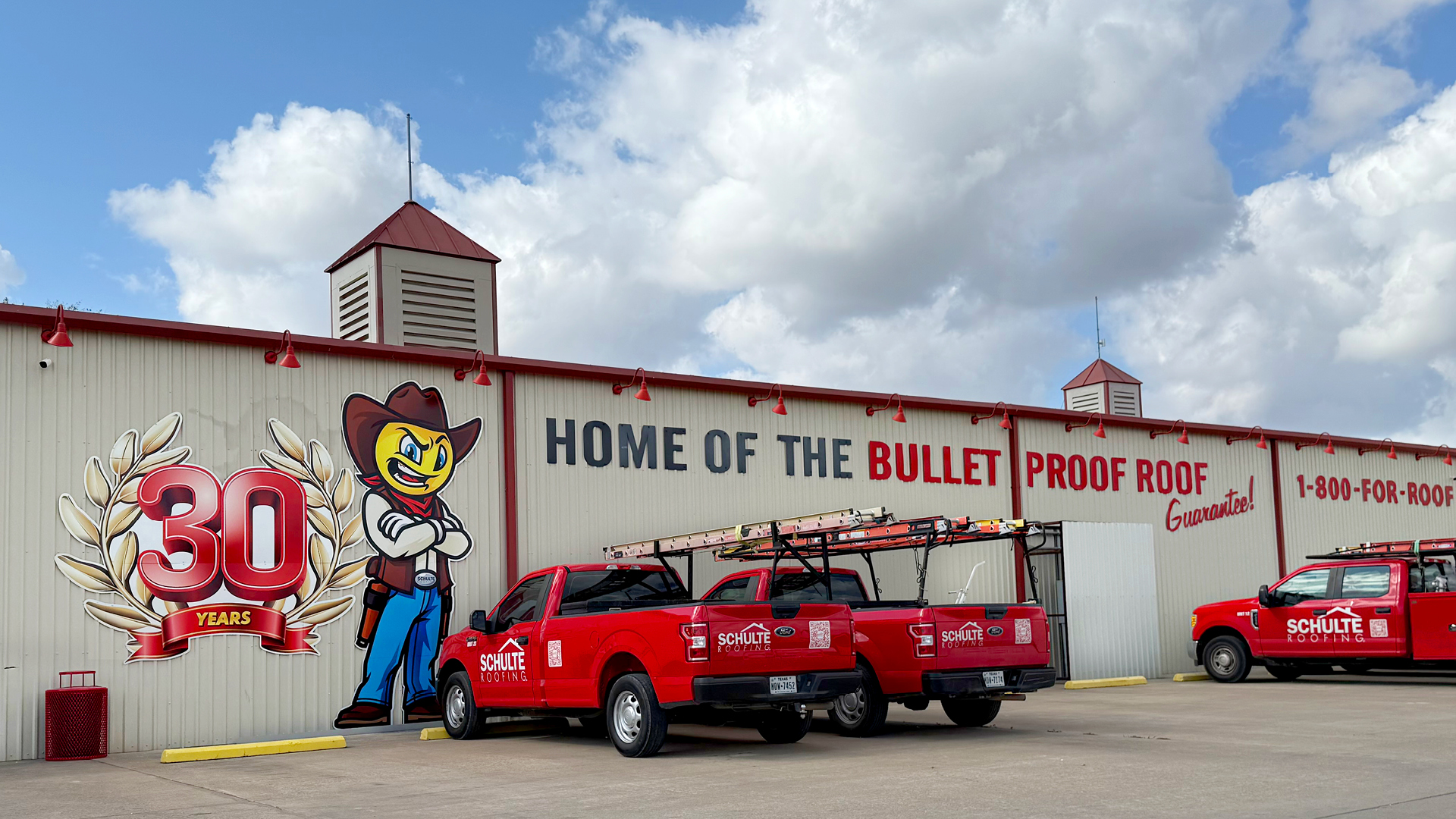 Schulte Roofing headquarters featuring a 30-year anniversary mural and company service trucks in Texas.